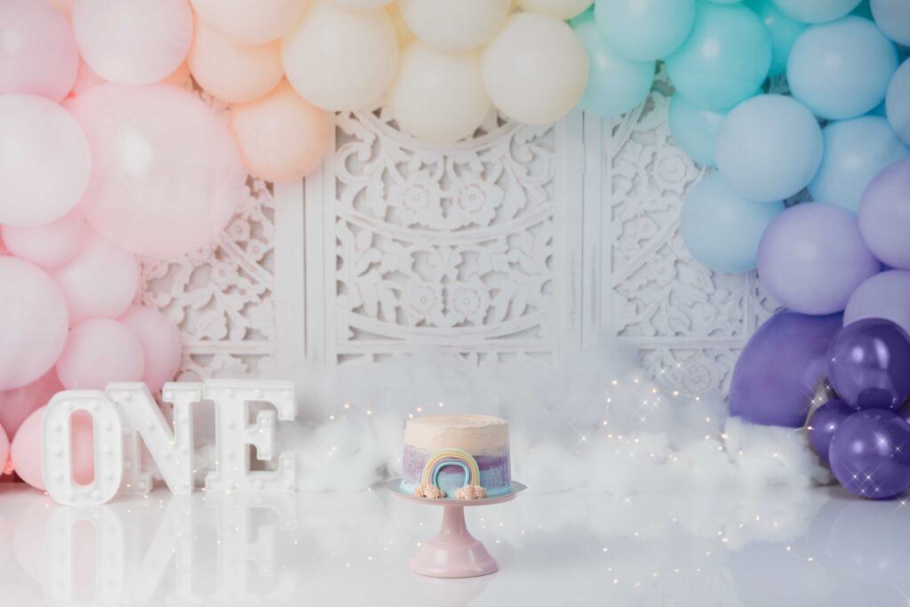 cakesmash in zachte regenboogkleuren met een ballonnenboog en de letters ONE
