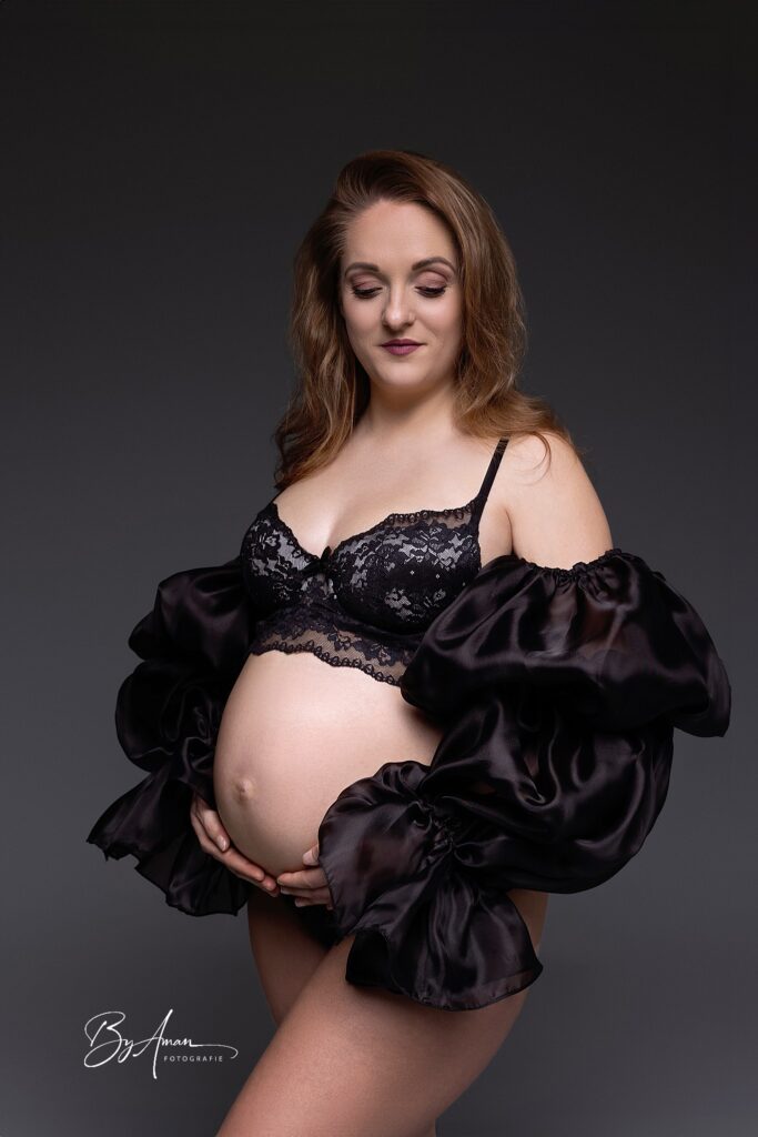 zwangere vrouw in zwarte lingerie met zwart voile mouwen tijdens studioshoot